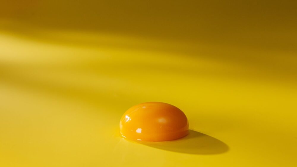 Egg yolk on a yellow surface with soft lighting.
