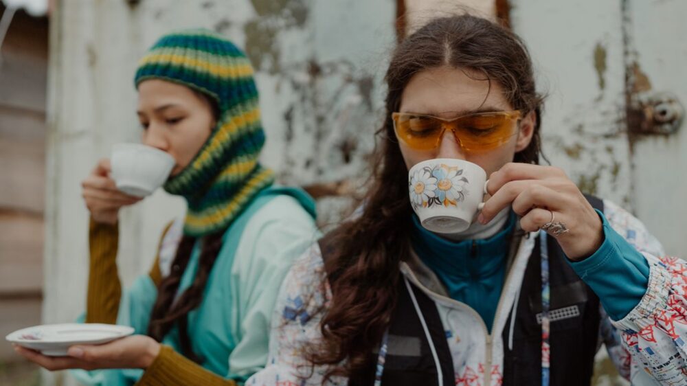Two people outdoors, drinking tea, wearing colorful winter clothing.
