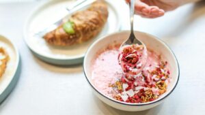 Bowl of pink yogurt with granola, croissant in background.