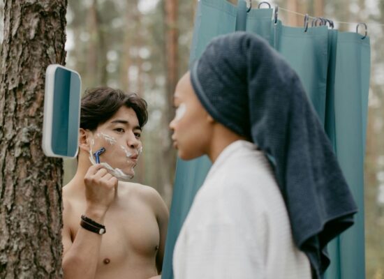 Two people grooming outdoors, one shaving, one with towel.