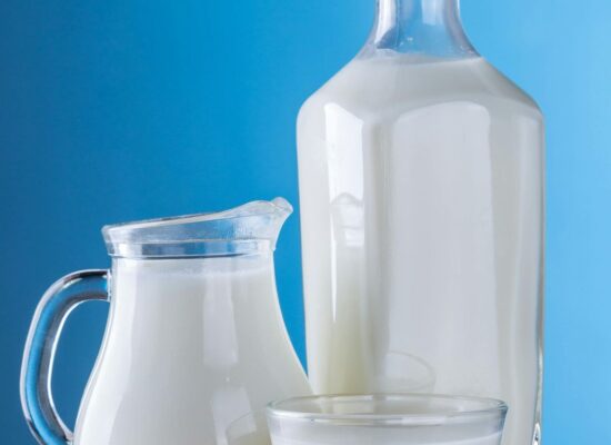 Glass bottle, jug, and cup filled with milk, blue background.