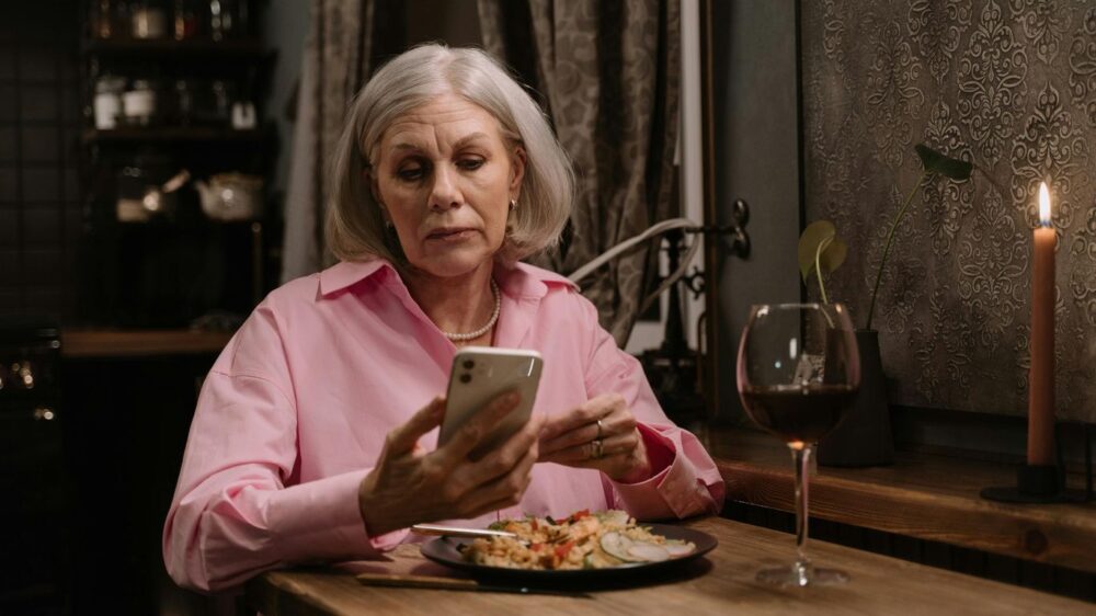Person sitting at table, eating dinner, looking at phone.