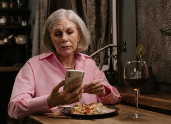 Person sitting at table, eating dinner, looking at phone.