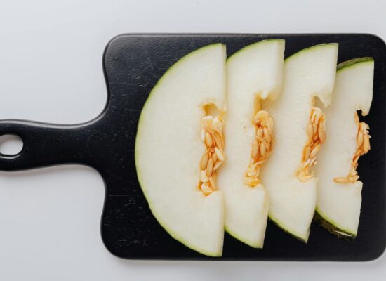 Four slices of melon with seeds on a black cutting board.
