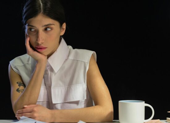 Person looking away from camera, resting chin on hand, with papers and mug.