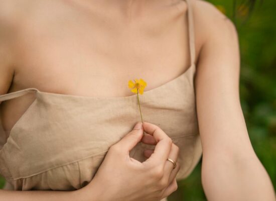 Person in beige dress holding small yellow flower to chest.