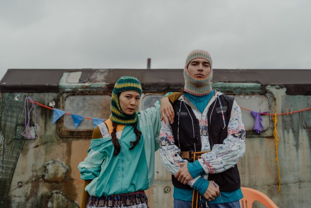Two people in colorful outfits stand in front of trailer.