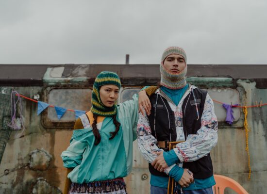 Two people in colorful outfits stand in front of trailer.